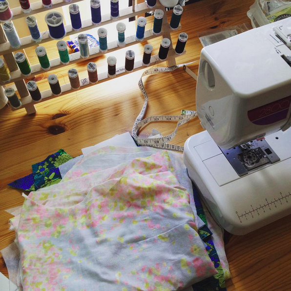 A sewing machine, fabric, and a thread rack full of colourful spools