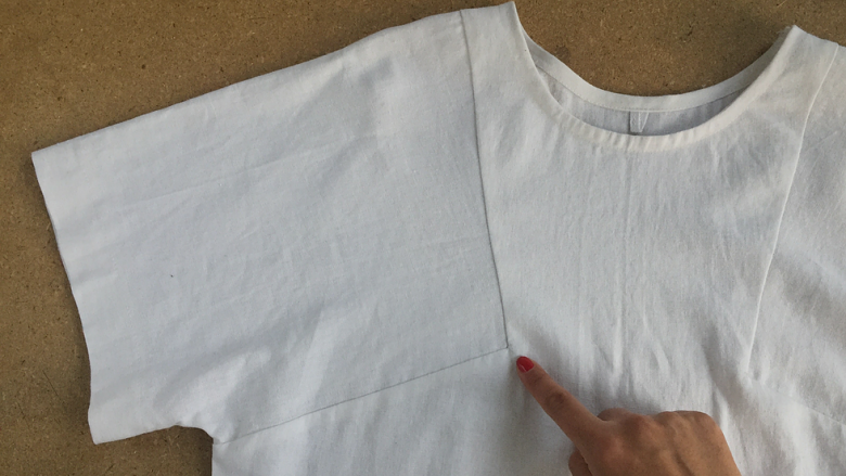 flat lay of garment with a hand pointing at the right corner of the sleeve seam