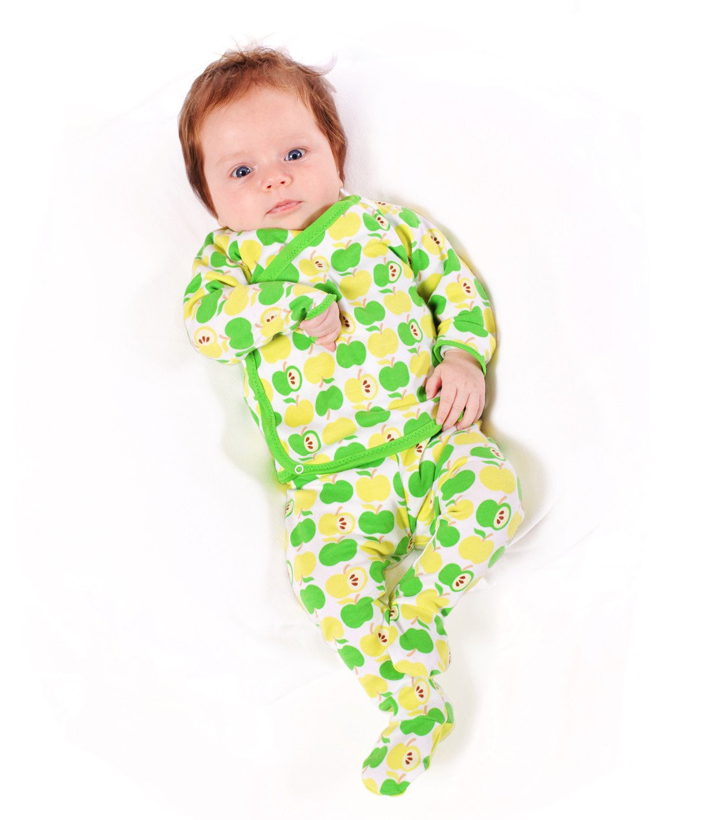 A baby wearing a cross-front shirt and footed leggings in a green apple print against a white background.