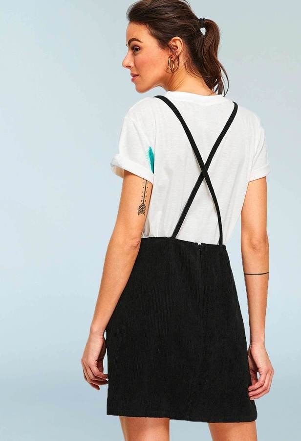 woman in a white tshirt and a black pinafore / overalls dress, back view showing crisscrossing straps
