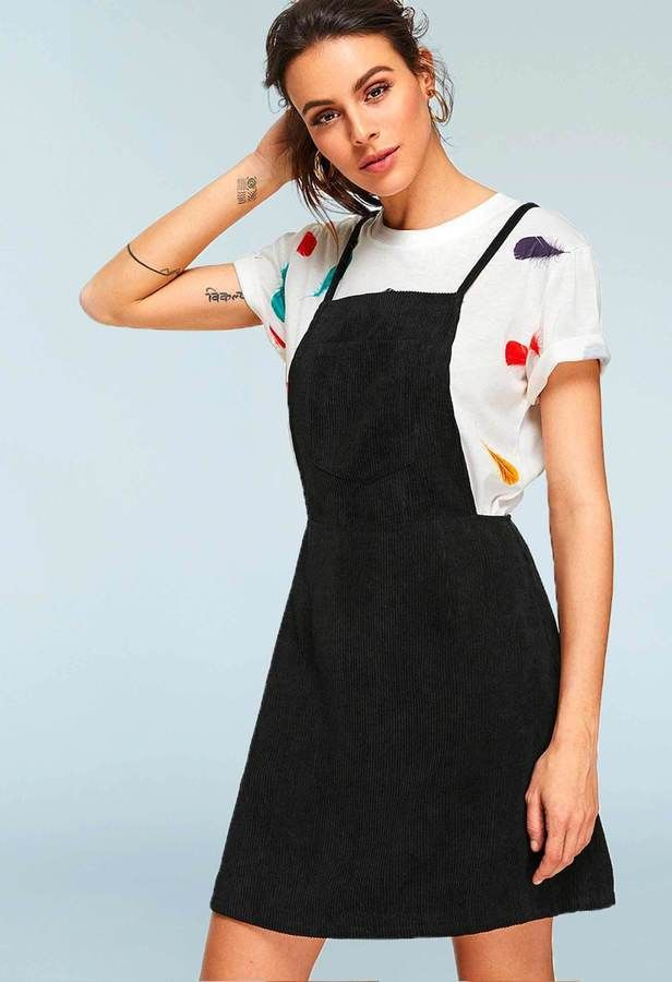 woman in a white tshirt and a black pinafore / overalls dress, front view, with hand on hair and at side