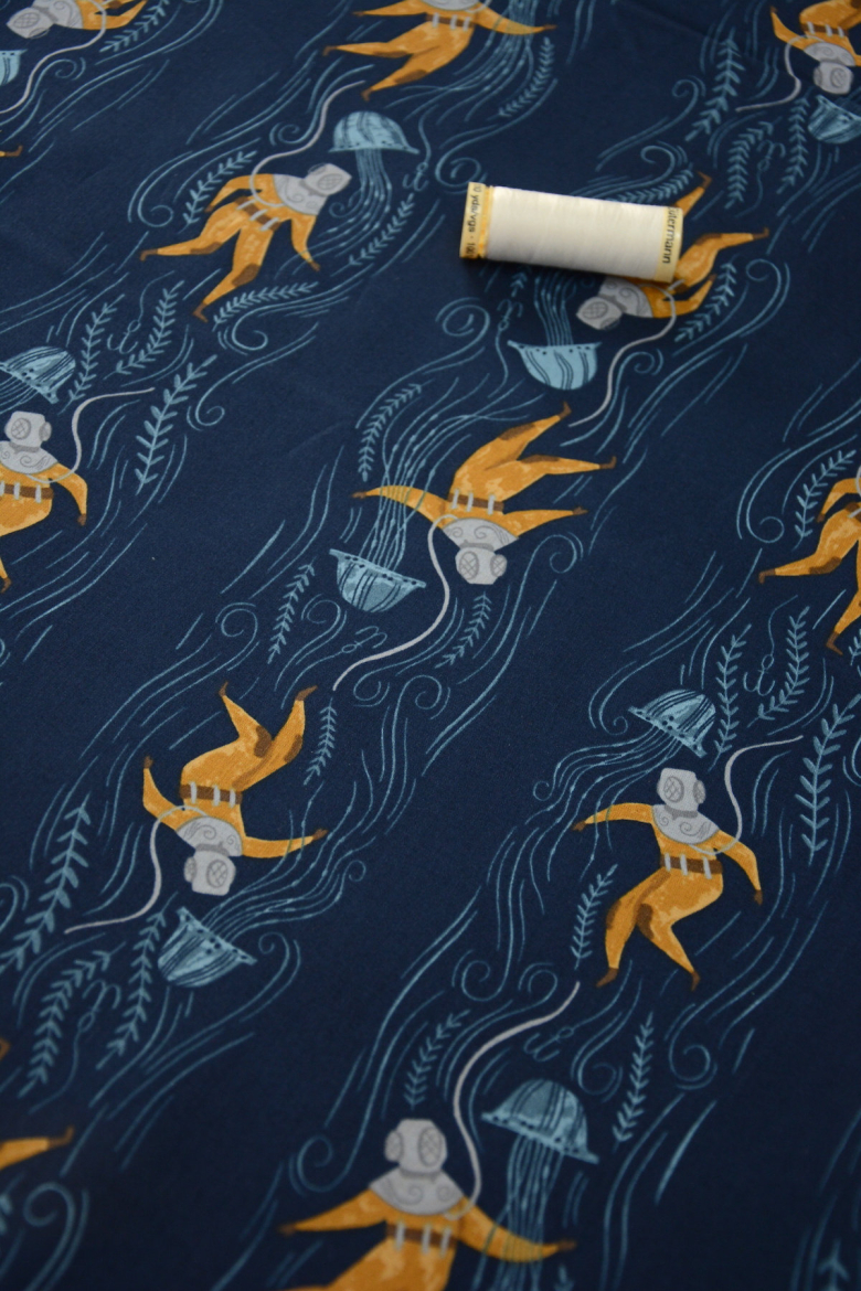 Deep sea divers on a navy background fabric with a thread of spool laying on top of the fabric