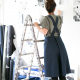 woman wearing apron dress on a ladder with her back to the camera