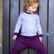A small child in a light, long-sleeved shirt and purple pants standing in front of a black door.