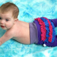 A baby, shirtless and wearing purple pants with pink and purple bum ruffles laying tummy down on a light blue cloth.