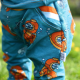 A close up showing a mock-pocket detail on a pair of teal and orange pants.
