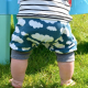A toddler, shown from the waist down, standing on grass and wearing a pair of shorts with white clouds against a dark blue ground.