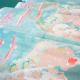 fabric on a cutting mat from an angle, showing fabric with an abstract floral print, in shades of aqua, peach, neon coral, and offwhite