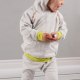 A small child wearing a grey and yellow hoodie and leggings against a grey wall.