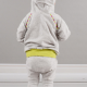 Backview of a small child wearing a grey and yellow hoodie and leggings against a grey wall.