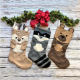 Three Christmas stocking with animal features - doe, racoon and bear - against a grey wooden background with a green garland and red box above.