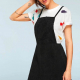 woman in a white tshirt and a black pinafore / overalls dress, front view, with hand on hair and at side