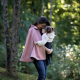 A woman wearing a hip length pink cape and holding a small child.