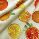White fabric with a pattern of  yellow and orange citrus fruits, with some folds