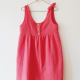 A pink sleeveless dress with front button placket hanging against a white wall.