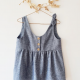 A grey sleeveless top with front button placket hanging against a white wall.