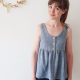 A woman in a grey sleeveless top with front button placket standing against a white wall.