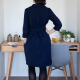 Back view of a woman in a navy blue wrap dress with three-quarter sleeves standing in front of a desk against a white wall.
