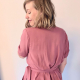 Back view of a woman in a pink, short sleeved wrap top in front of a white wall.
