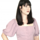 white woman with dark hair wearing a mauve button-down top with puffy elbow-length sleeves