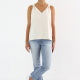 Image features a Caucasian woman posing in a white v-neck tank top with delicate ribbon detail at the shoulders, a pair of light wash jeans, and a pair of tennis shoes.