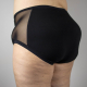 A person wearing black, super high rise undies with mesh side panels, viewed from the side back