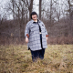 A fat Asian woman standing in nature wearing a grey checked shirt jacket.