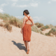 Back view of a woman in a red dress standing on a sandy hill.