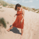 Front view of a woman in a red dress standing on a sandy hill.