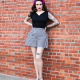 Front view of woman standing with hands on hips in black top and wide black and white shorts in front of brick wall