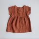 A brown baby dress laid flat on a grey background. The dress has a plain bodice with cut on, short sleeves and a gathered skirt.