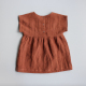 A brown baby dress laid flat on a grey background. The dress has a plain bodice with cut on, short sleeves, snaps closing the centre back, and a gathered skirt.