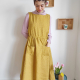 Image of a woman with short brown hair wearing a sleveeless dress with pockets in a yellow linen fabric