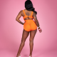 Back view of a black woman wearing an orange a white swimsuit standing against a pink background. Her hair is pulled over her shoulder to show off the back fastener on the swimsuit.