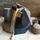 A square bottomed drawstring bag on a wooden surface next to a pincushion and spool of thread. The bag is blue, linen, yellow and red.