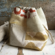 A square drawstring bag sitting on a wooden surface with a skein of cream coloured yarn. The bag is made with a patchwork of linen, yellow and red printed fabrics.