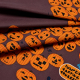 Jack-O-Lantern Poplin.  A fabric printed with dark mauve background with a pile of orange jack-o-lantern pumpkins with a sign reading &amp;quot;Pumpkin Carving Contest&amp;quot;. A skeleton trick-or-treater in and oversized blue shit is holding a jack-o-lantern to the right of the pile