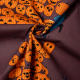 Jack-O-Lantern Poplin.  A fabric printed with dark mauve background with a pile of orange jack-o-lantern pumpkins with a sign reading &amp;quot;Pumpkin Carving Contest&amp;quot;. A skeleton trick-or-treater in and oversized blue shit is holding a jack-o-lantern to the right of the pile