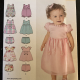 The front of the pattern envelope shows ten pieces in different fabric colors on the left side and an image of a young toddler wearing a pink outfit on the right. The various outfits have rose accents like trim around the neck and sleeves and large flowers hanging on ribbons off the waist seam.