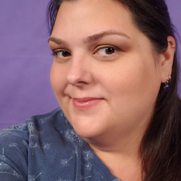 White woman with dark hair and eyes with a smirk, wearing a navy shirt