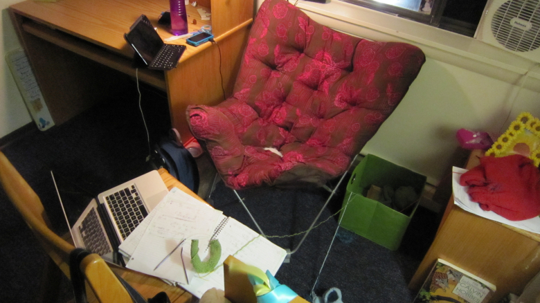 pink and brown store-bought butterfly chair in college, surrounded by books, technology, and knitting projects